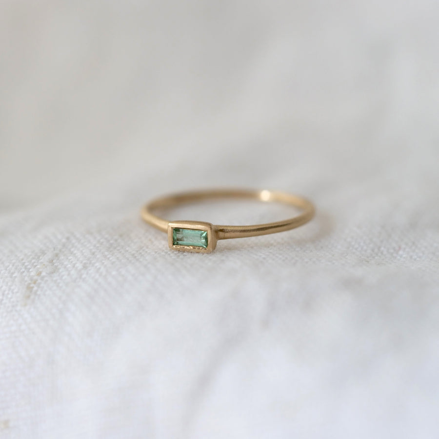 Gold ring with a green gemstone on a white fabric background