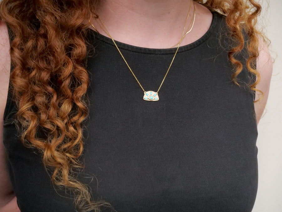 Person wearing a black top and gold necklace with a green pendant