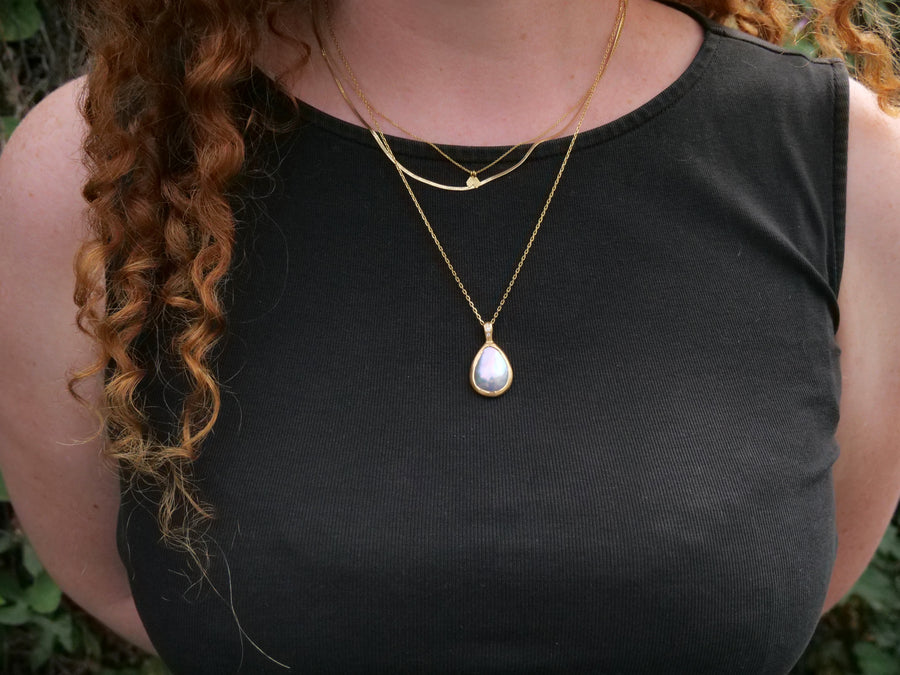 Person wearing a black sleeveless top with gold necklaces and a pendant.