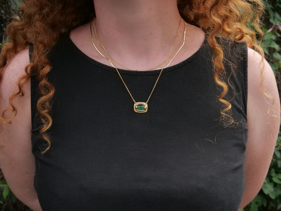 Person wearing a black top and gold necklace with a green pendant outdoors