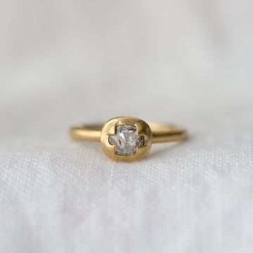 Gold ring with a light grey diamond prong set in gold on a white fabric background