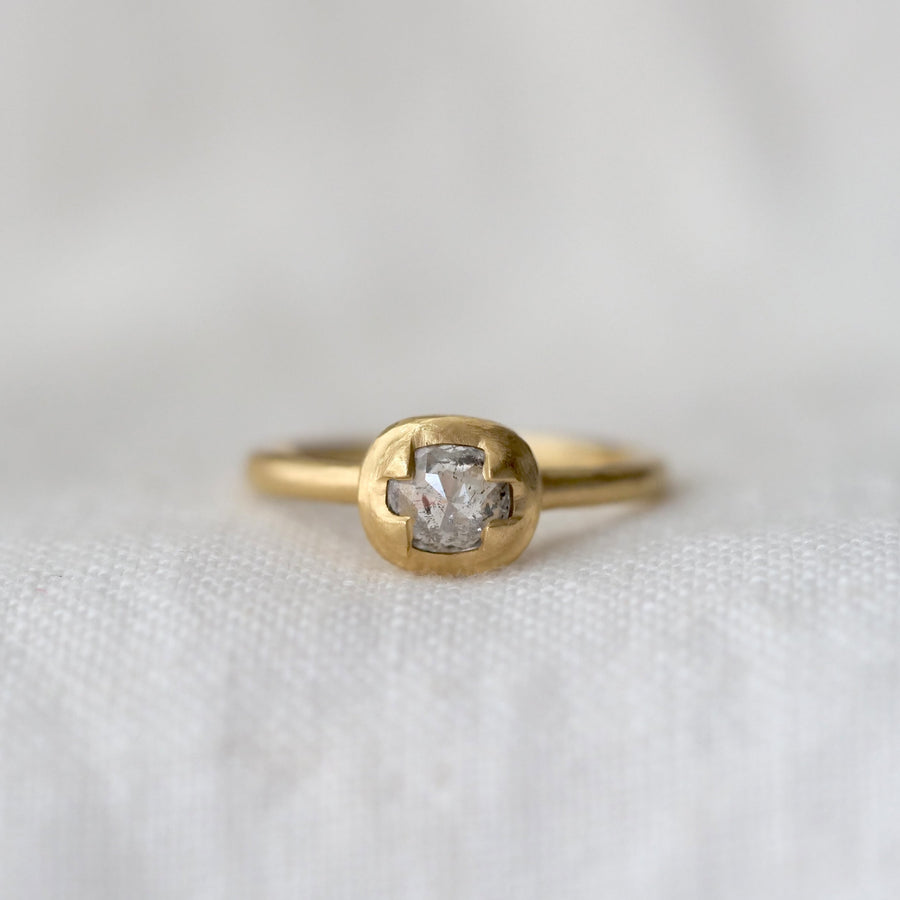 Gold ring with a light grey diamond prong set in gold on a white fabric background