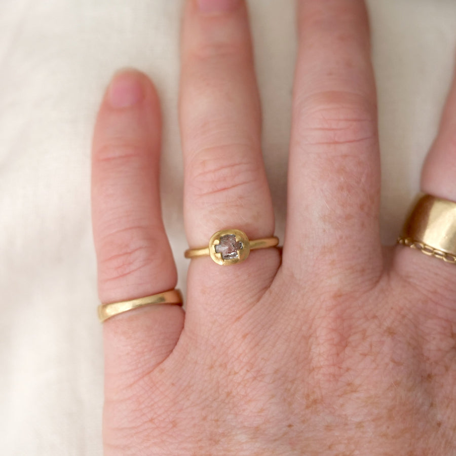 Hand wearing two gold rings with a clear gemstone on a neutral background