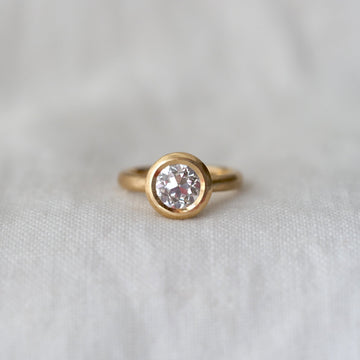 Gold ring with a large lab diamond bezel set in gold, on a white fabric background