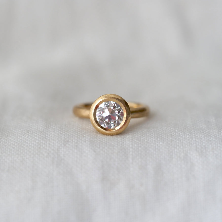 Gold ring with a large lab diamond bezel set in gold, on a white fabric background