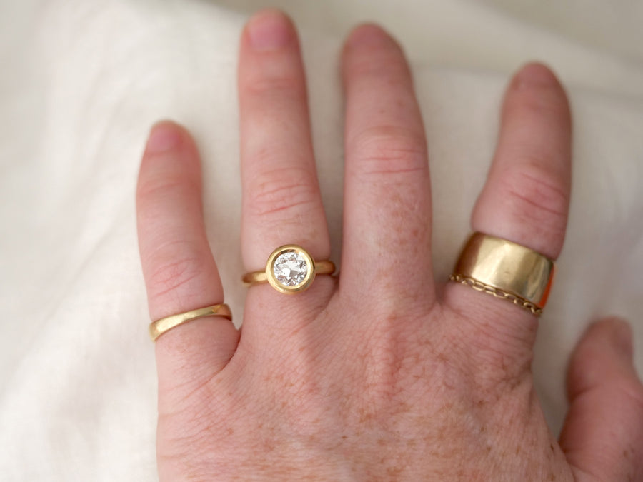 Hand wearing two gold rings with a clear gemstone on a white background