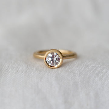 Gold ring with a bezel set white diamond on a light gray background