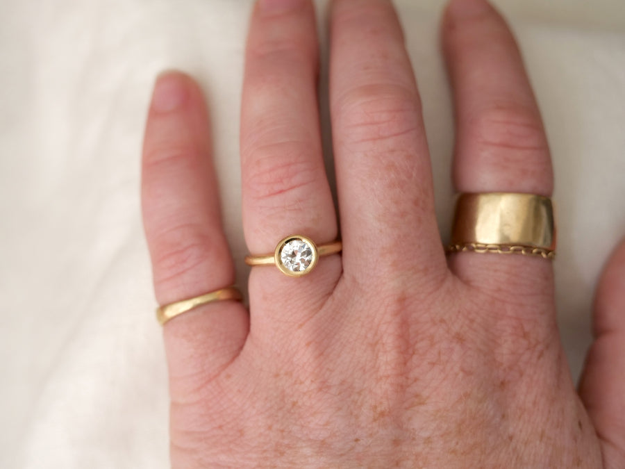 Hand wearing two gold rings with a white stone on a light background