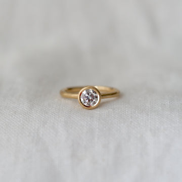 Gold ring with a white diamond bezel set, on a light fabric background