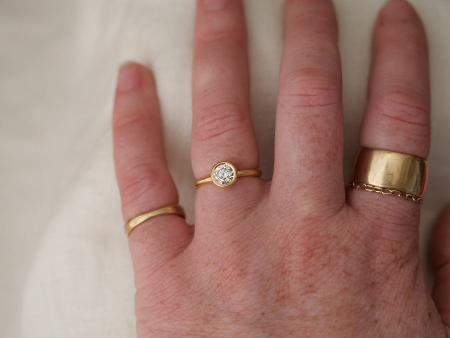 Hand wearing two gold rings with a diamond on a neutral background
