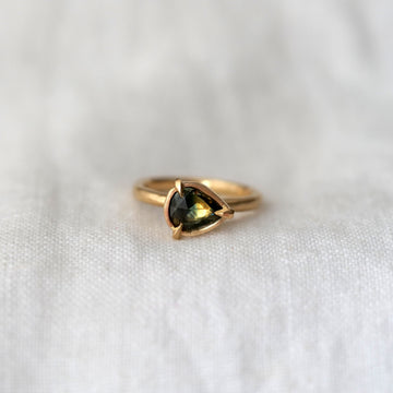 Gold ring with a green pear shaped sapphire gemstone prong set, on a white fabric background