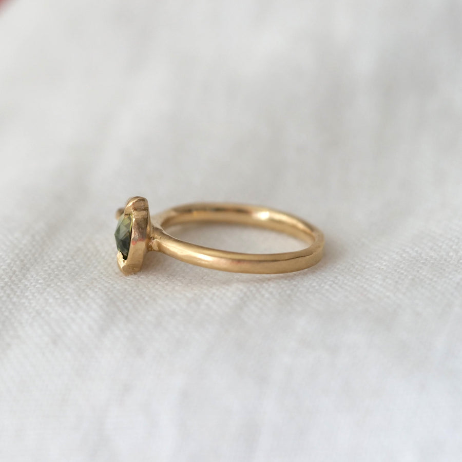 Gold ring with a green gemstone on a white fabric background