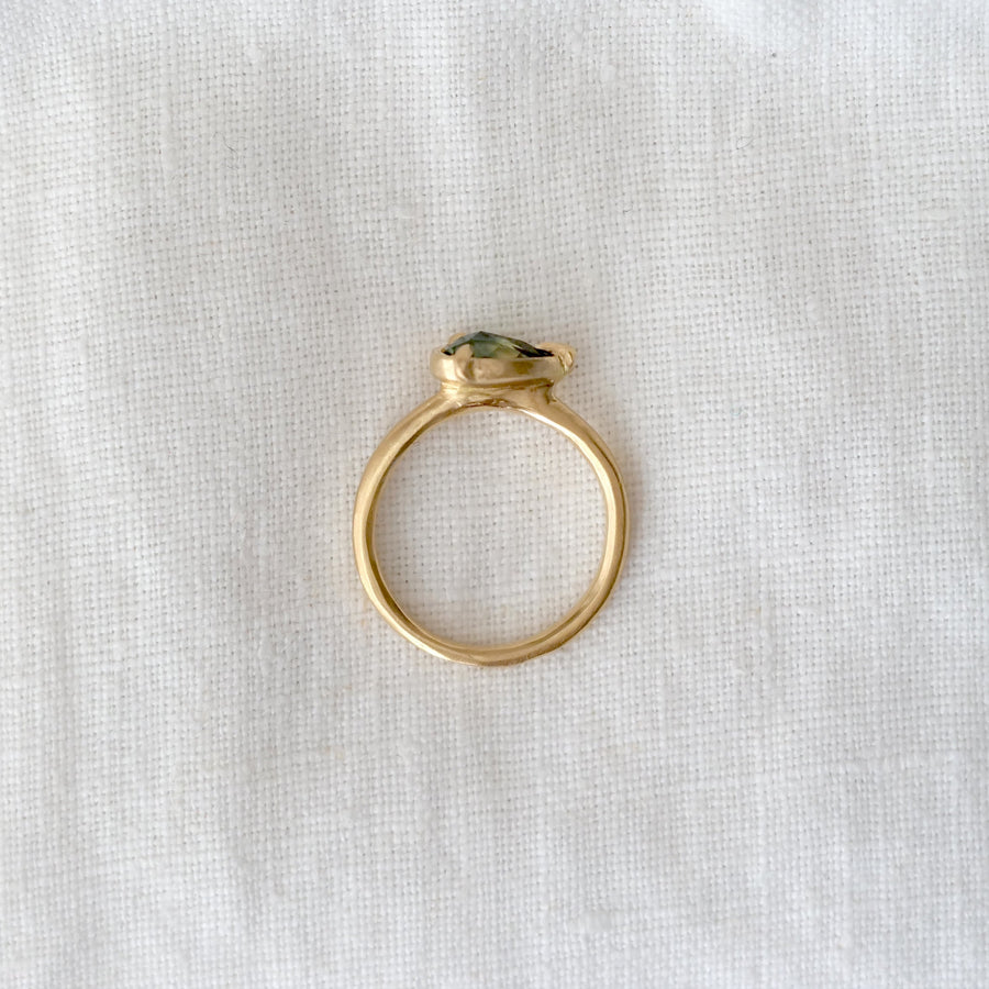 Gold ring with a green gemstone on a white fabric background