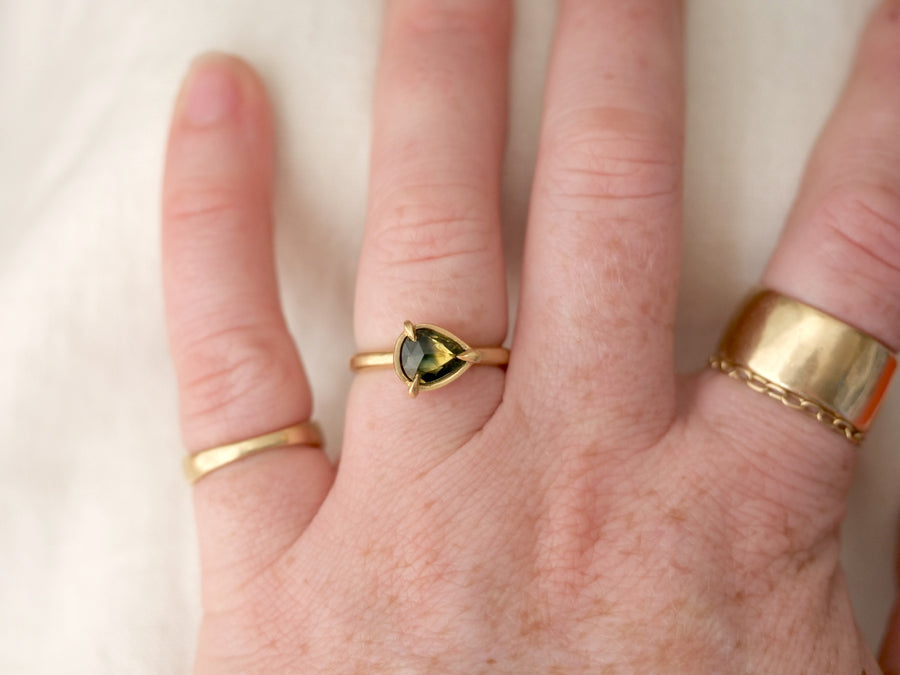 Hand wearing two gold rings with a heart-shaped gemstone on a light background