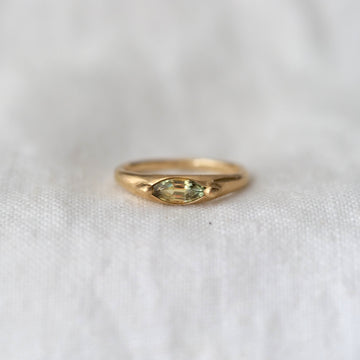 Gold ring with a green marquise cut gemstone on a white fabric background