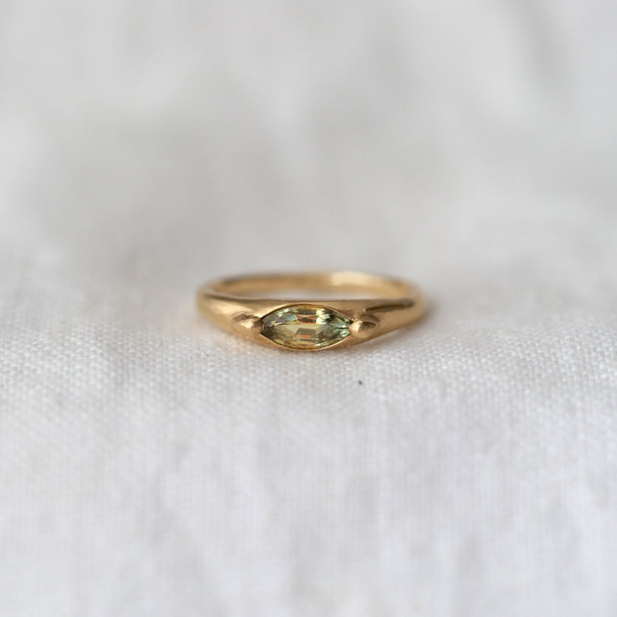 Gold ring with a green marquise cut gemstone on a white fabric background