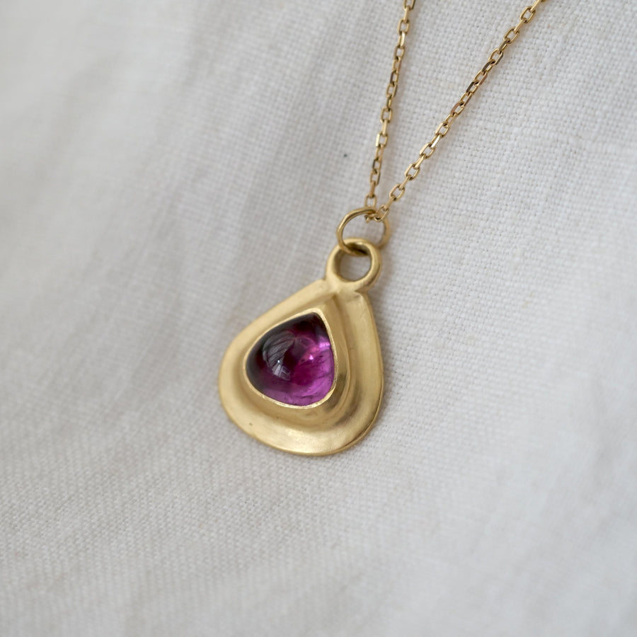 Gold pendant with a purple gemstone on a light gray background