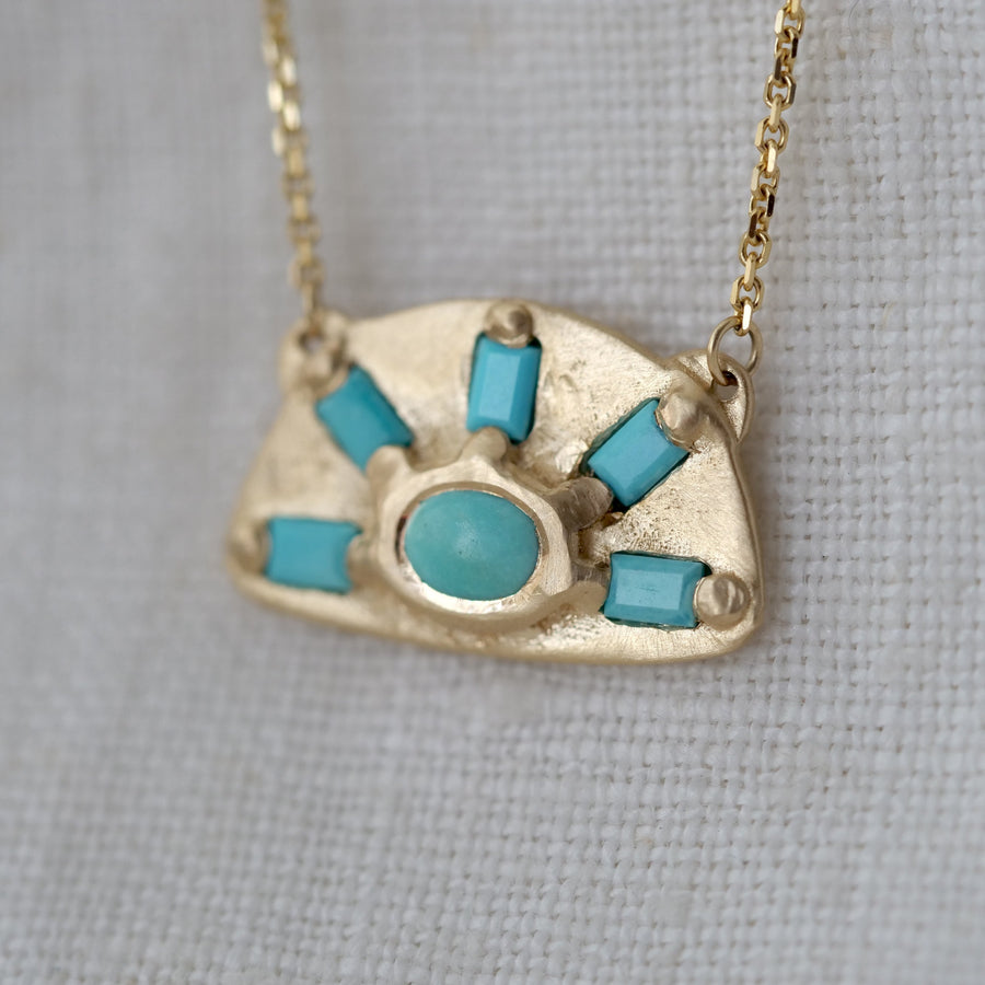 Gold necklace with turquoise stones on a gray fabric background