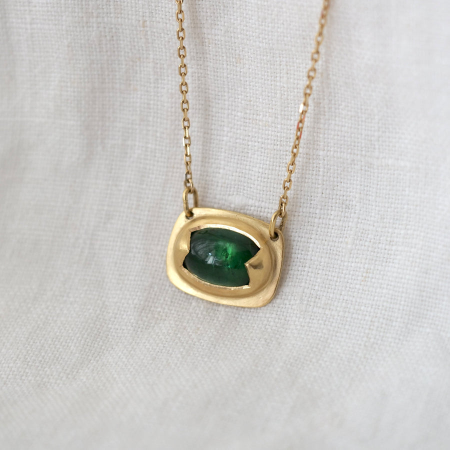 Gold necklace with a green gemstone pendant on a white fabric background