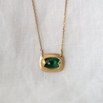 Gold necklace with a green gemstone pendant on a light fabric background