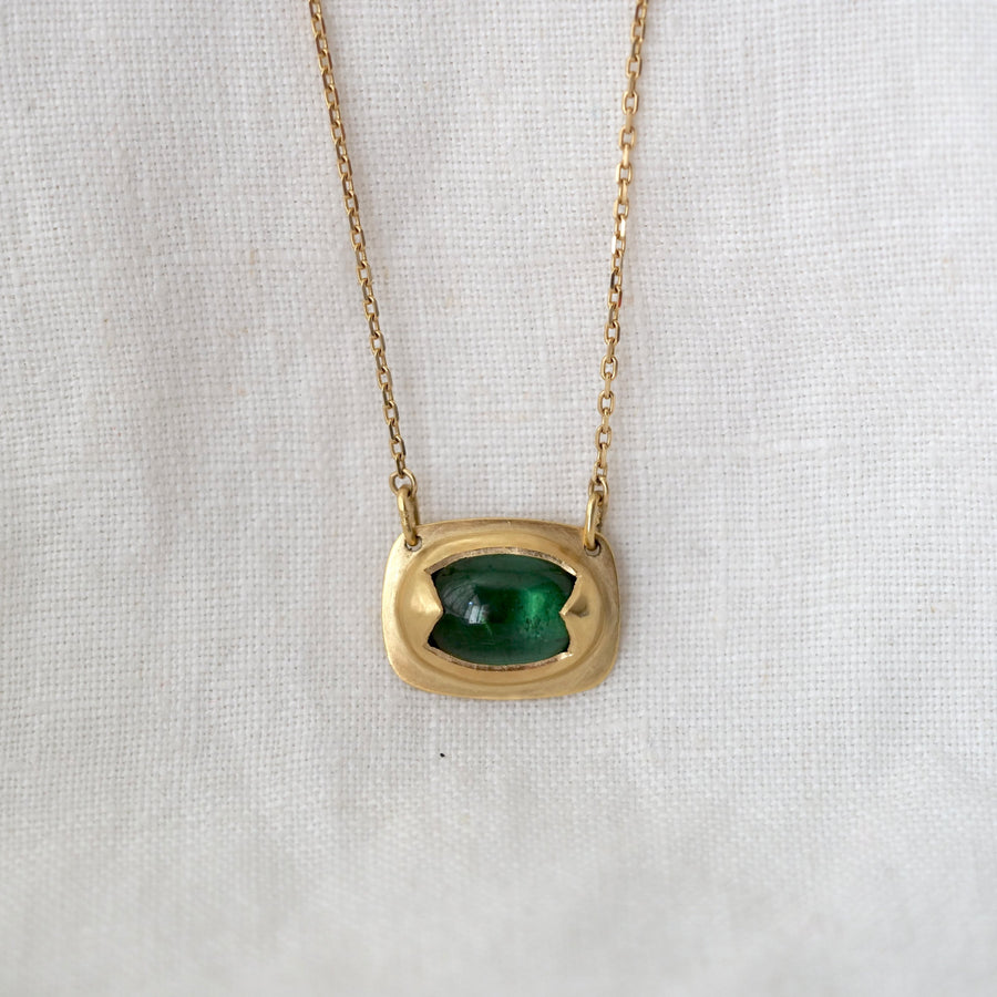 Gold necklace with a green gemstone pendant on a light fabric background