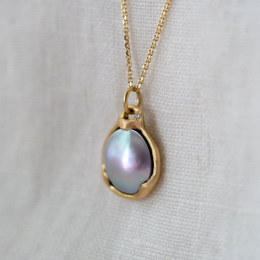 Gold necklace with a teardrop-shaped pearl pendant on a light gray background