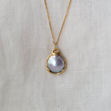 Gold necklace with a pearl pendant on a light gray background
