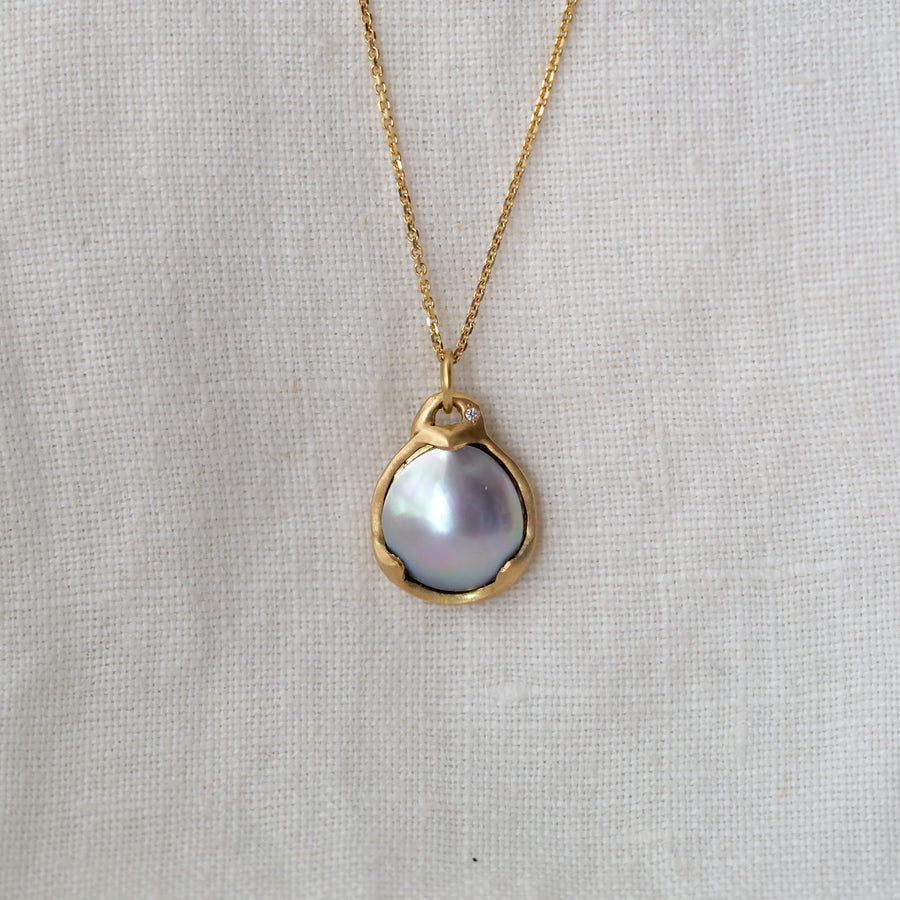 Gold necklace with a pearl pendant on a light gray background