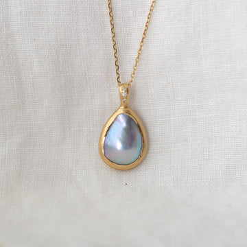 Gold necklace with a teardrop-shaped pearl pendant on a light fabric background