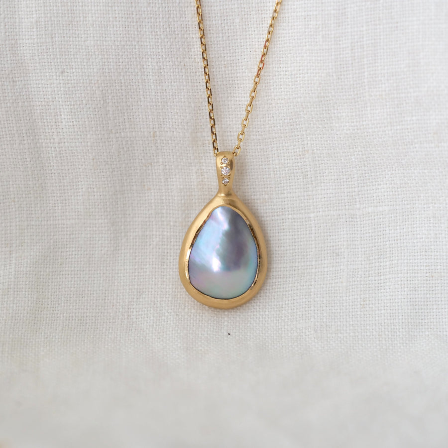 Gold necklace with a teardrop-shaped pearl pendant on a light fabric background