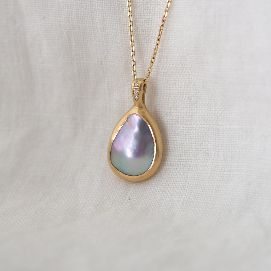 Gold necklace with a teardrop-shaped pendant on a light fabric background
