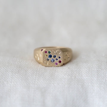 Gold square signet ring with colorful gemstones on a white fabric background