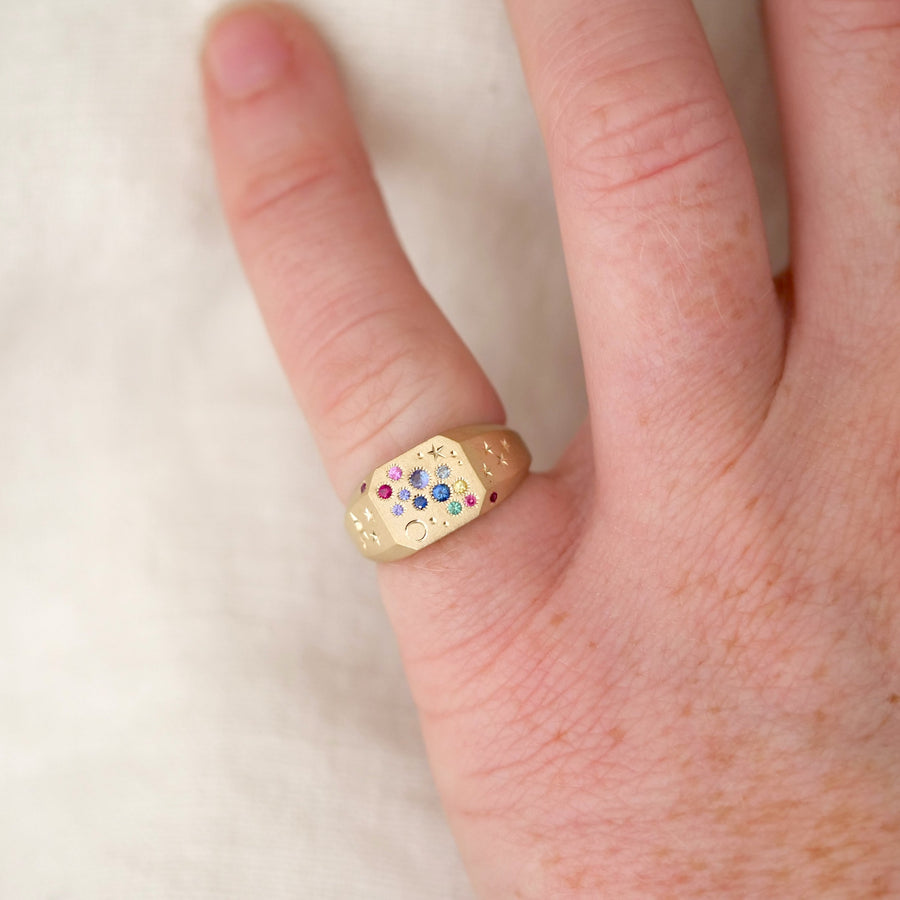Gold ring with colorful gemstones on a finger against a white background