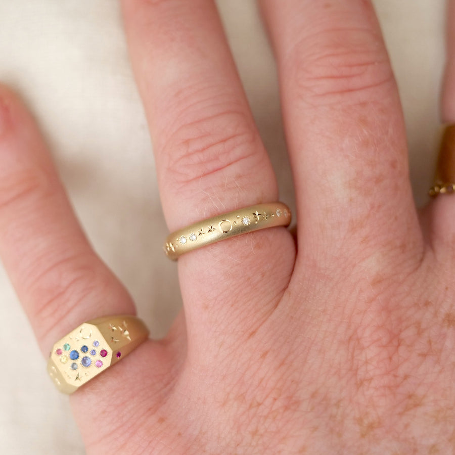 Close-up of a hand wearing two gold rings with intricate designs on a light background