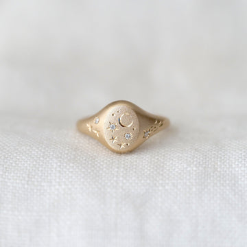 Gold ring with intricate moon and star design on a white fabric background