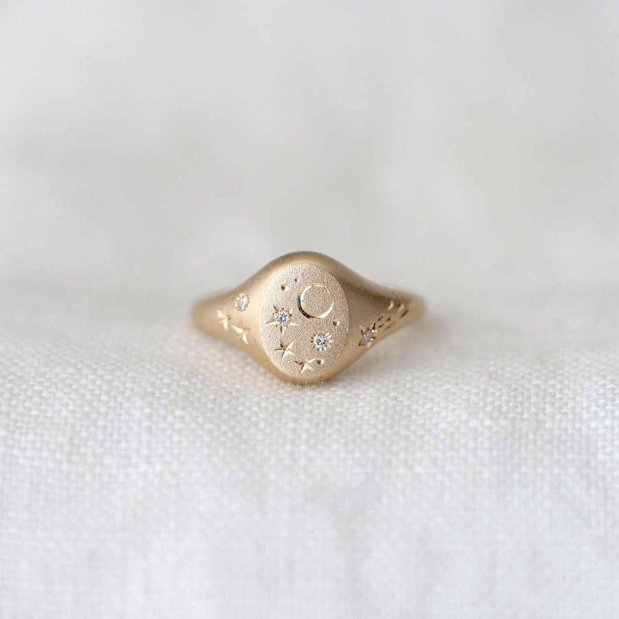 Gold ring with intricate moon and star design on a white fabric background