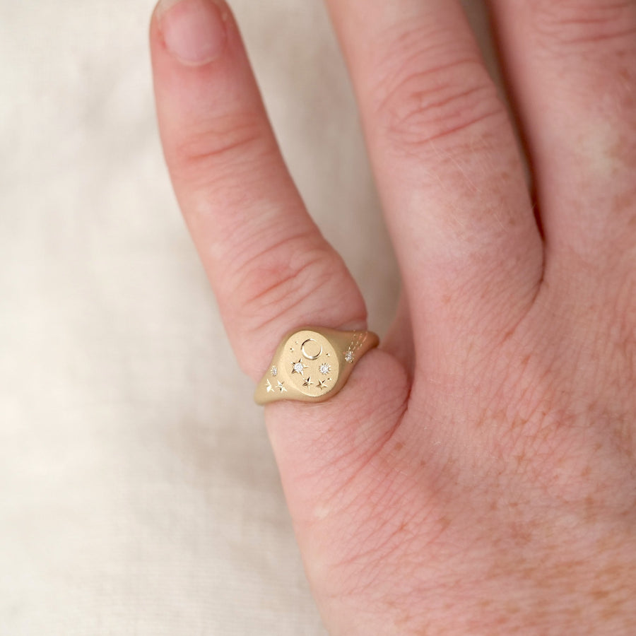 Gold ring with a heart design on a person's finger against a neutral background
