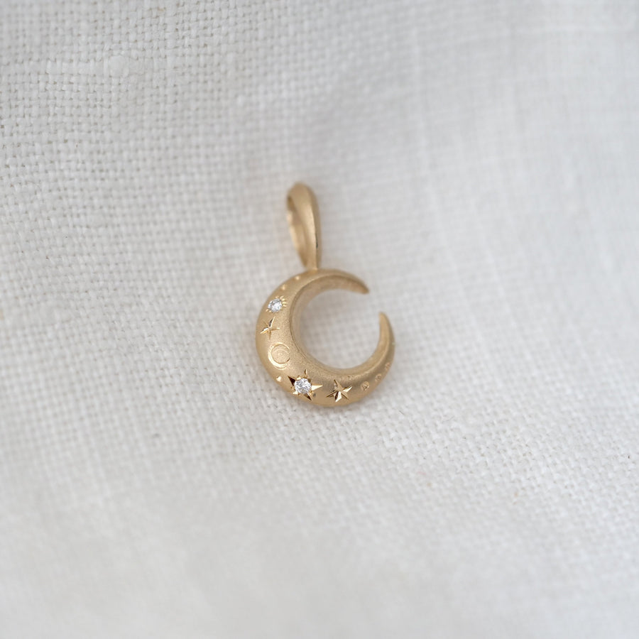 Gold crescent moon pendant with small stones on a white fabric background
