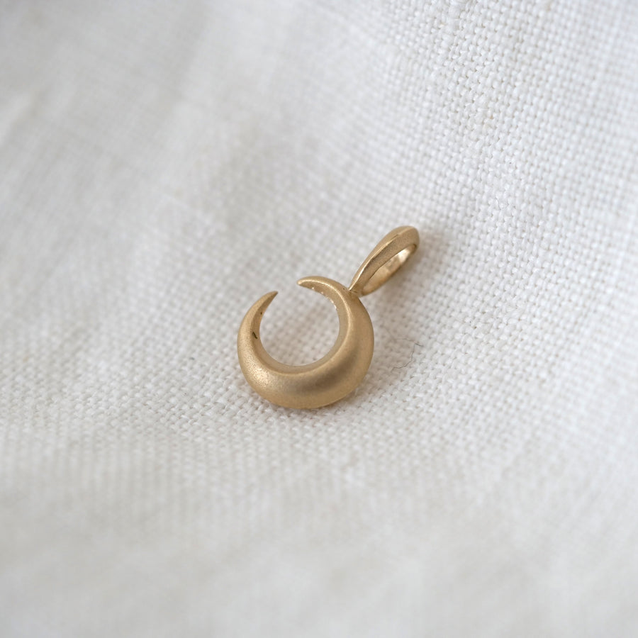 Gold crescent moon pendant on a white fabric background