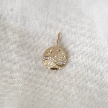 Gold pendant with star and moon design on a white fabric background