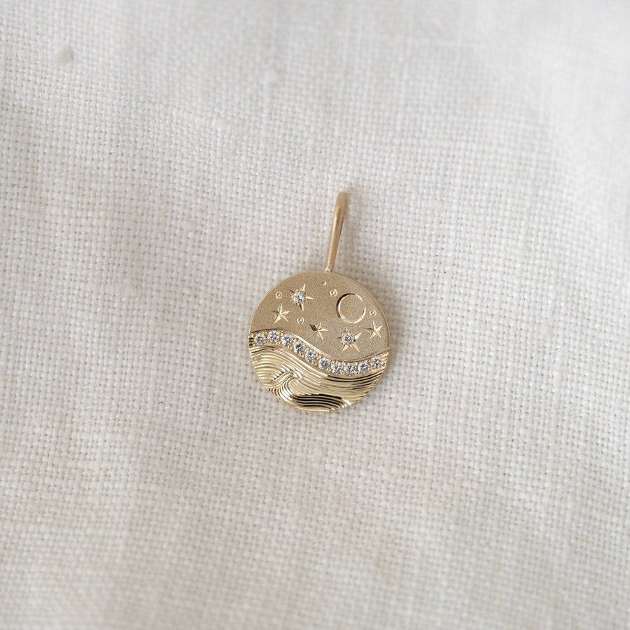 Gold pendant with star and moon design on a white fabric background
