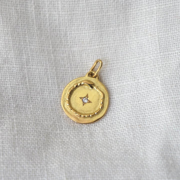 Gold pendant with a diamond on a light gray fabric background