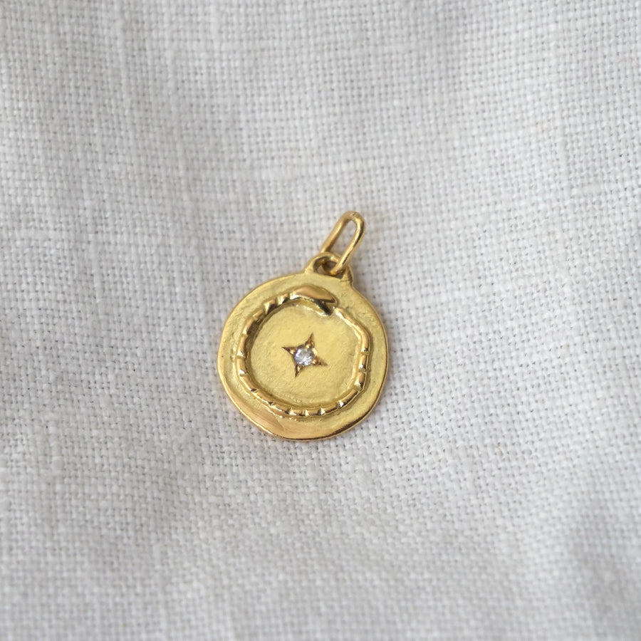 Gold pendant with a diamond on a light gray fabric background