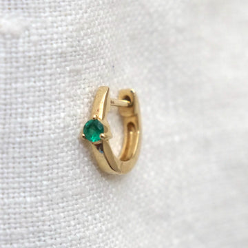 Gold hoop earring with a green gemstone on a white fabric background