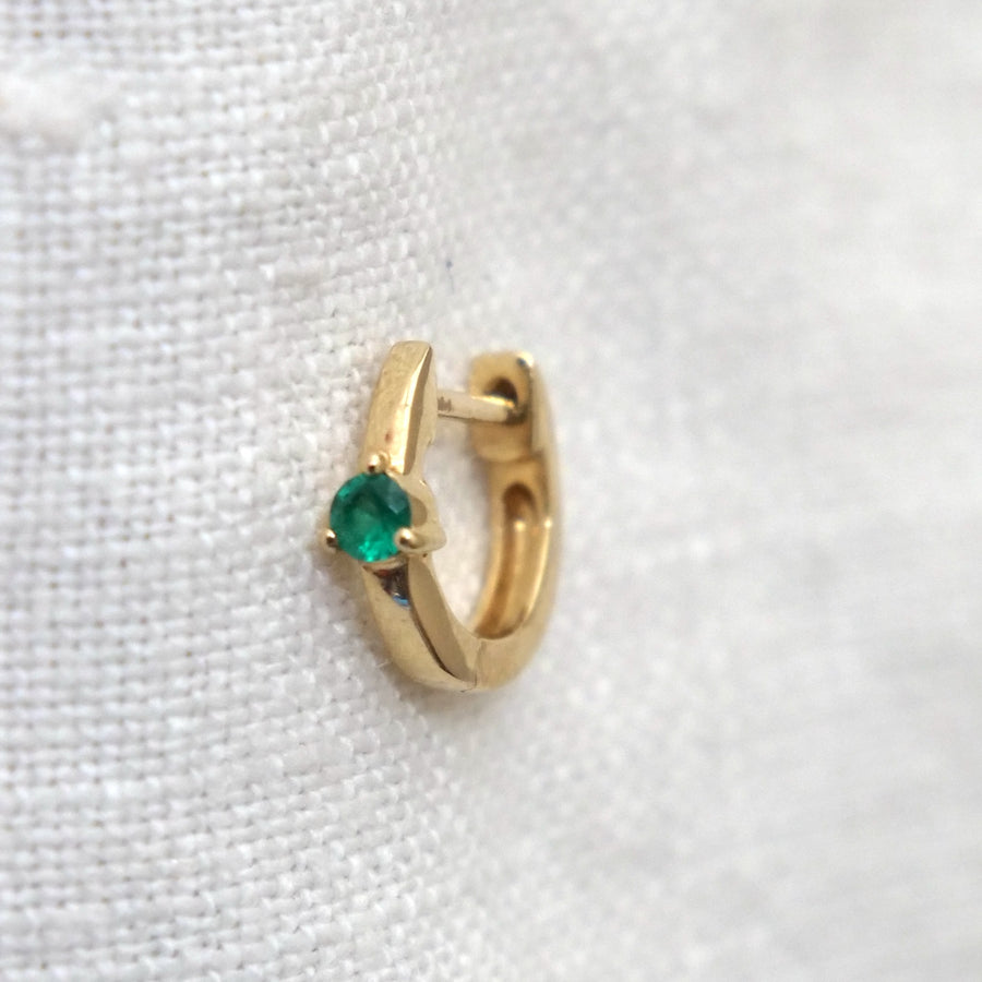 Gold hoop earring with a green gemstone on a white fabric background