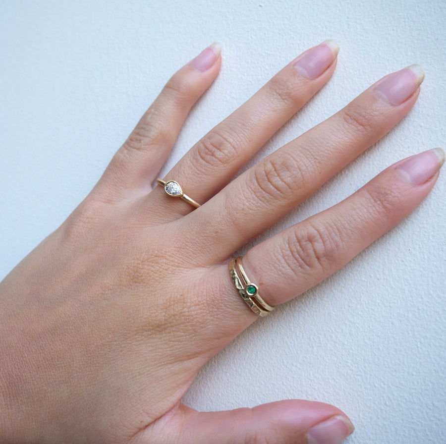 Hand wearing two gold rings with gemstones on a light background