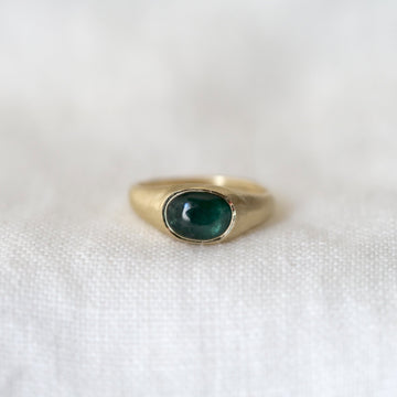 Gold ring with a deep green gemstone on a white fabric background