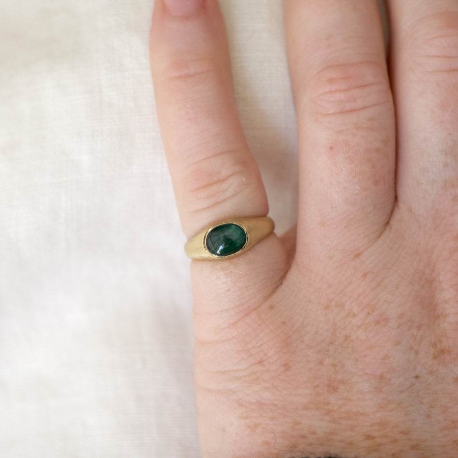 Gold ring with a green gemstone on a finger against a white background