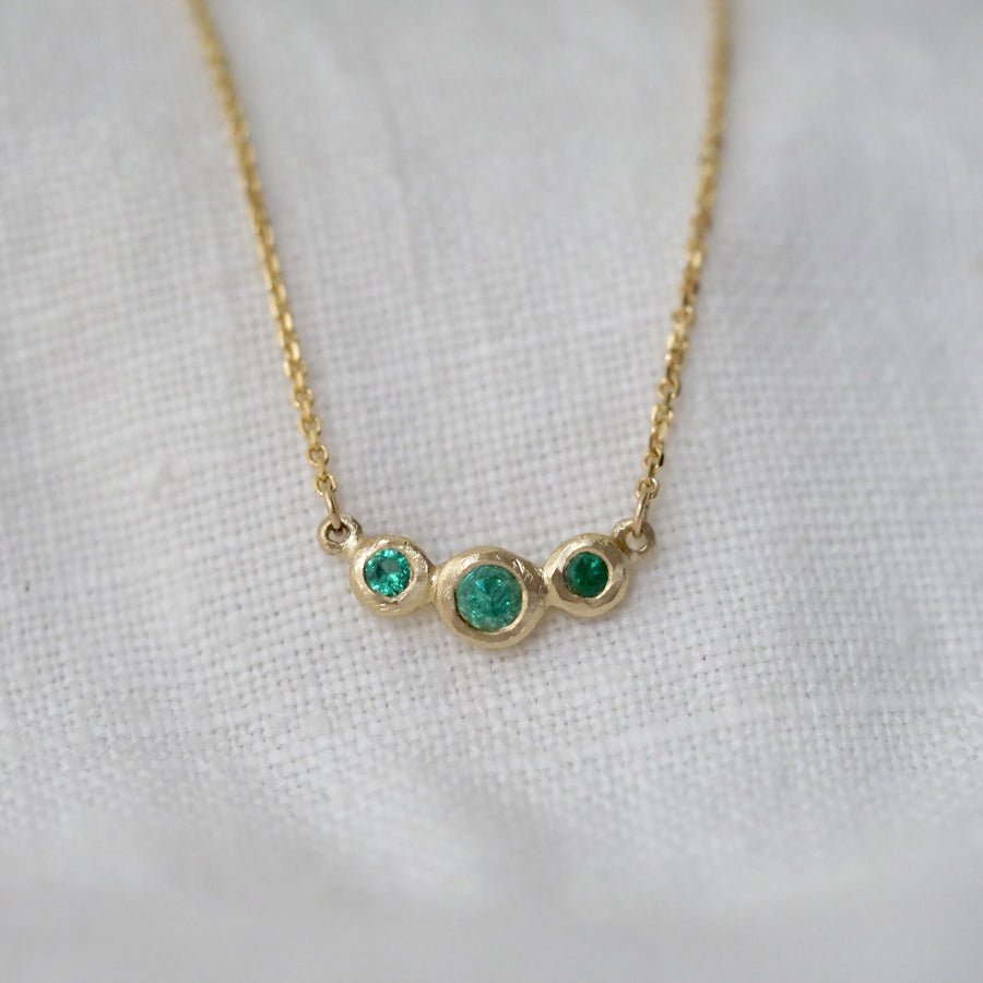 Gold necklace with three emerald stones on a light gray background