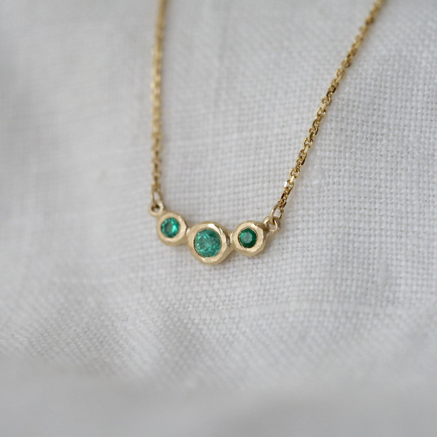 Gold necklace with three green gemstones on a light gray background